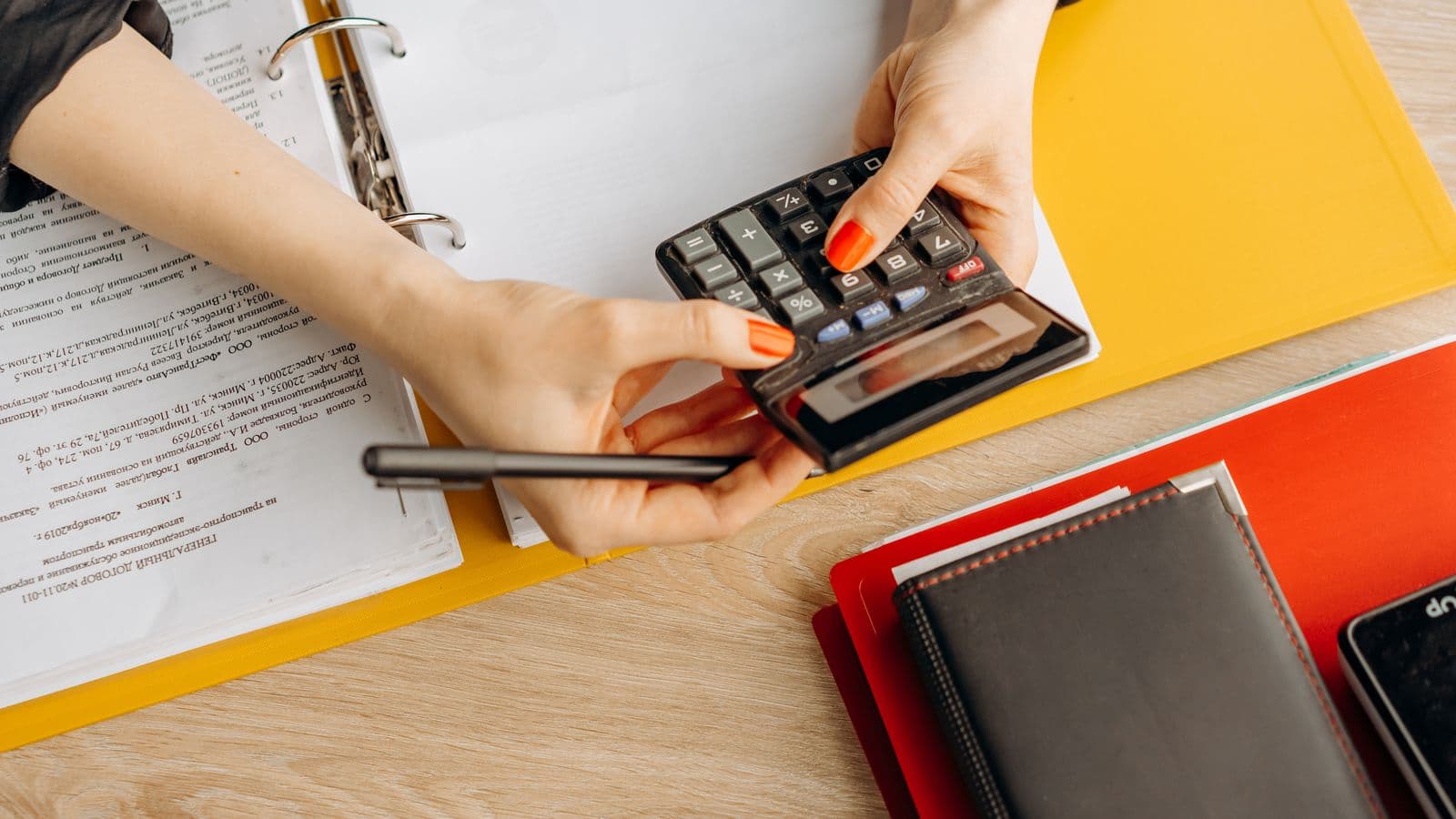 Mains d'un artisan calculant le coût de revient d'un chantier à la calculatrice avec des documents