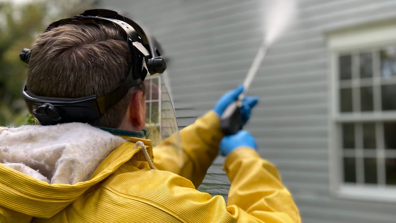 Personne en tenue de protection nettoyant la façade d'une maison au nettoyeur