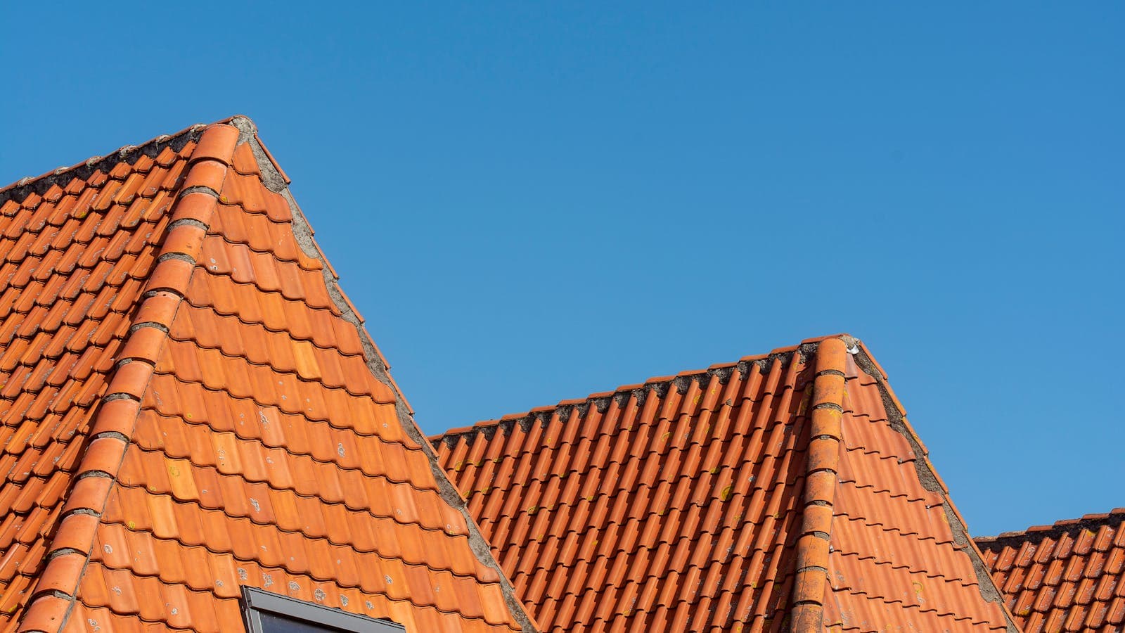 Toiture en tuiles rouges sous un ciel bleu, prête pour un nettoyage de toiture